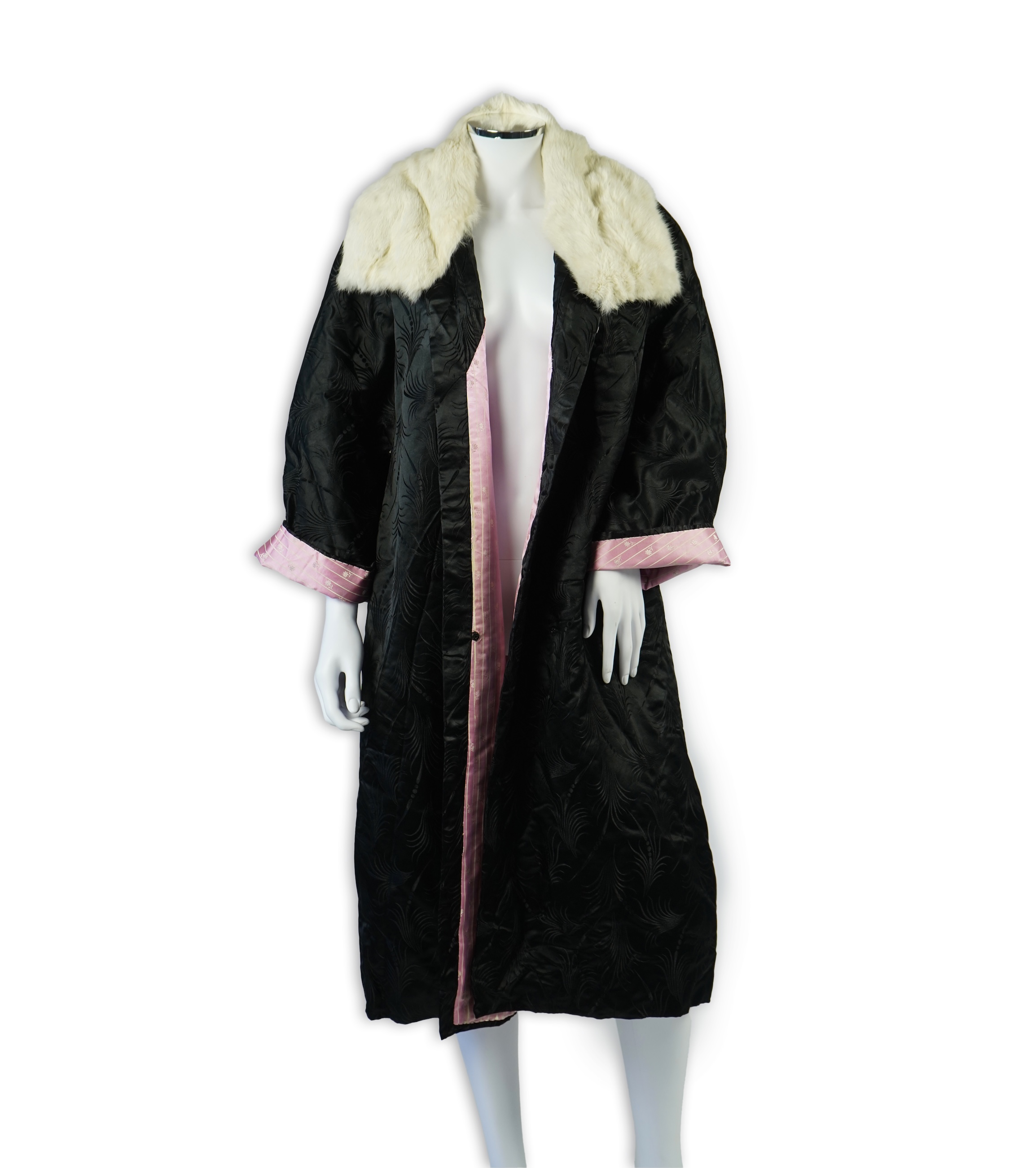 A 20th century ladies black silk damask opera coat, trimmed with a white fur collar and pink silk stripe brocade lining. 116cm from shoulder to hem. Condition - seams unstitched in places, small nick to black brocade by